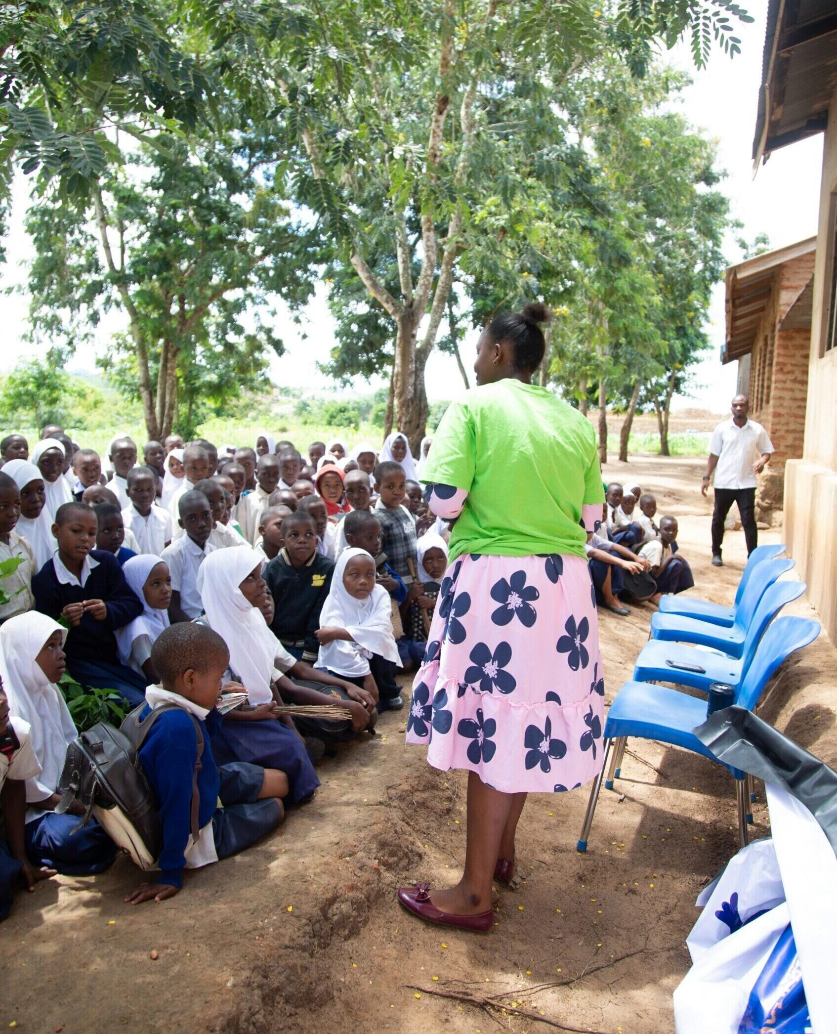 Teacher conducts outdoor lesson with attentive children under trees.